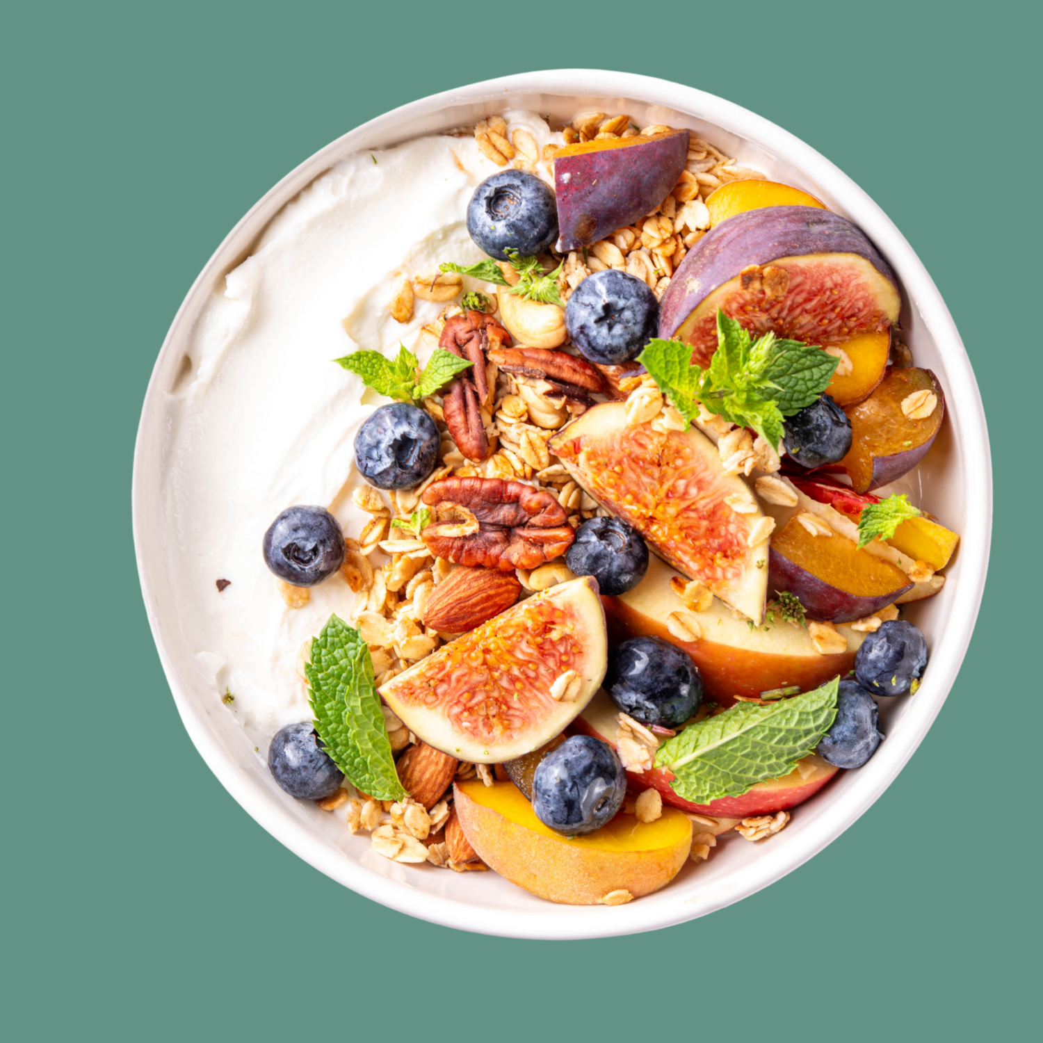 Bowl of yogurt with fruit (blueberries, fig, apple and peaches), nuts (almond, walnut and cashews) and some mint leaves.